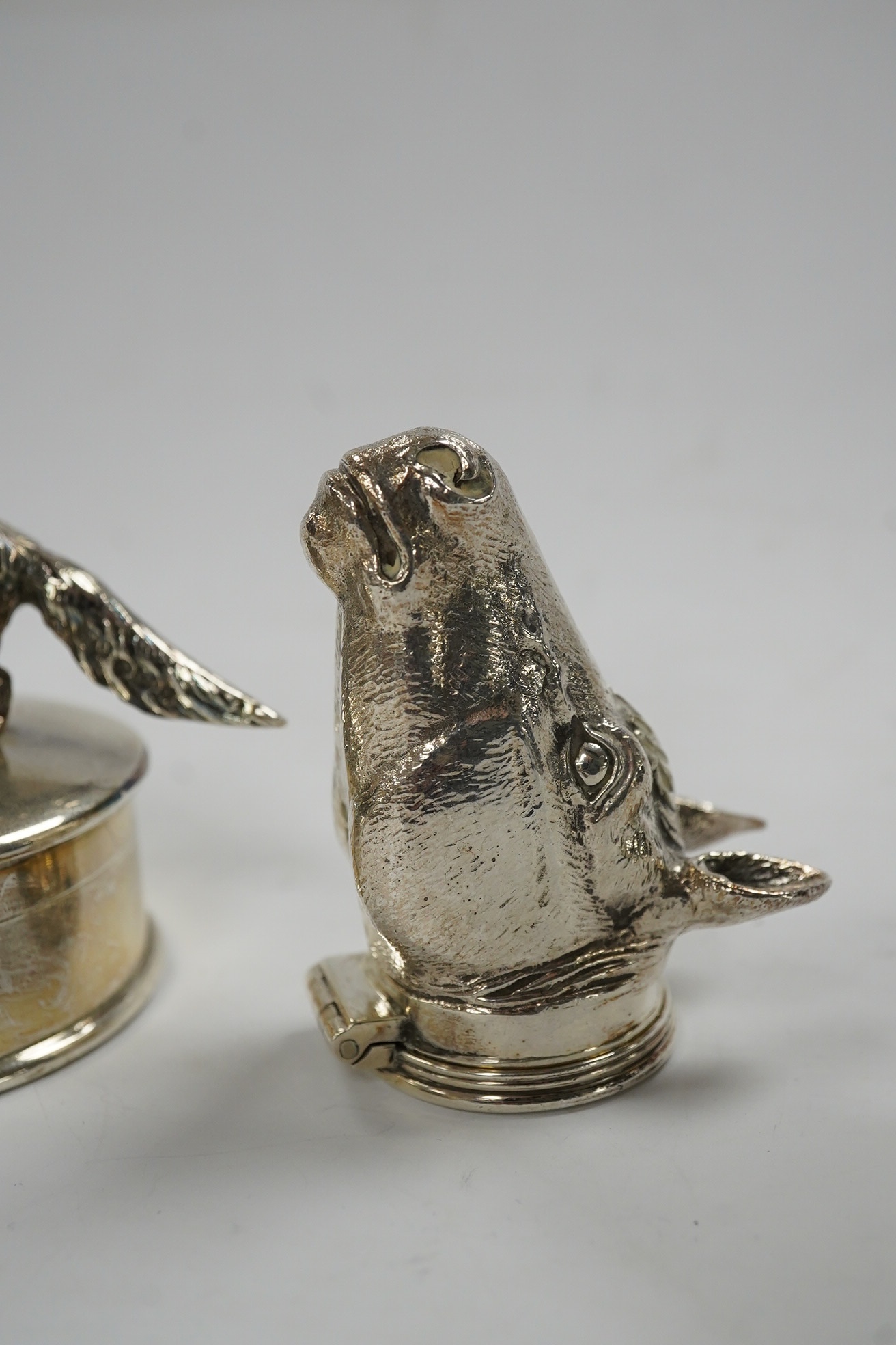 A George VI silver napkin ring modelled as a stirrup, surmounted with a fox, Birmingham, 1937, 46mm, together with a later silver horses head snuff box and a silver pill box with fox surmount. Condition - fair to good